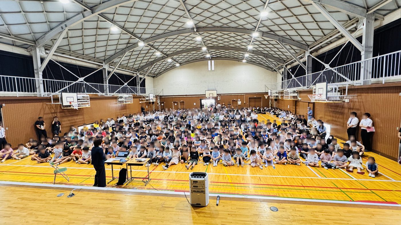 体育館いっぱいに座る児童と、まわりを囲む保護者・地域のみなさん